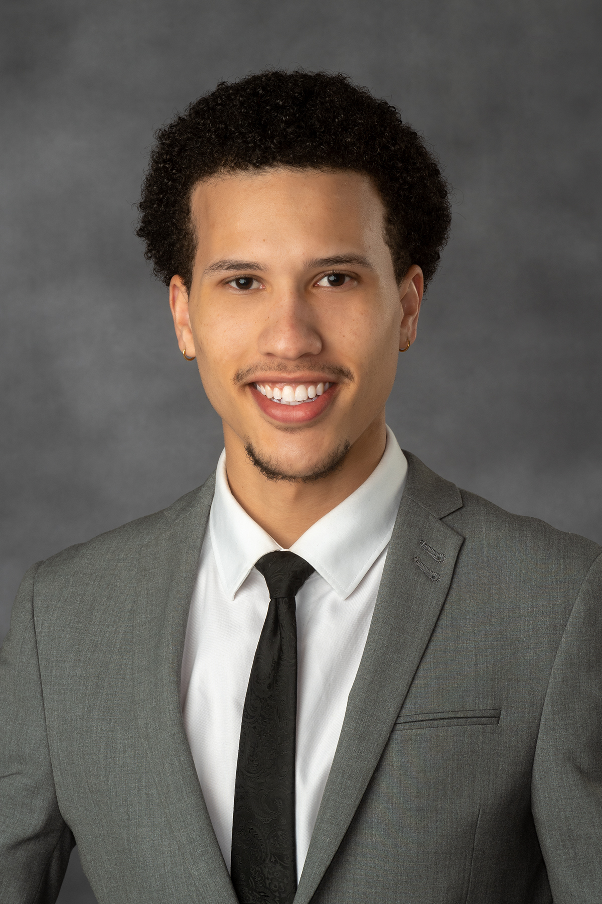 Headshot of Holden Spence from the shoulders up smiling in a business casual jacket and necktie.